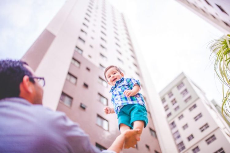 father holds toddler in palm lifting toward skyscrapers