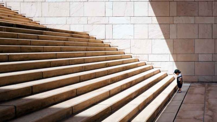 a toddler child stands at the bottom of imposing stone staircase at museum